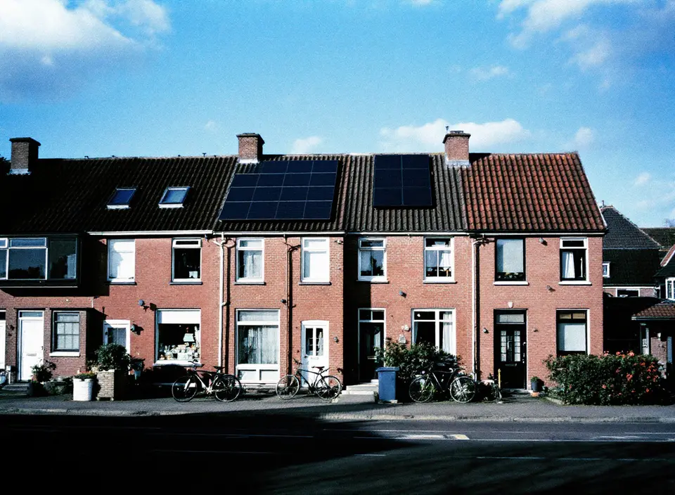 Een rij bakstenen rijtjeshuizen met zonnepanelen op de daken, fietsen tegen de gevels, blauwe lucht